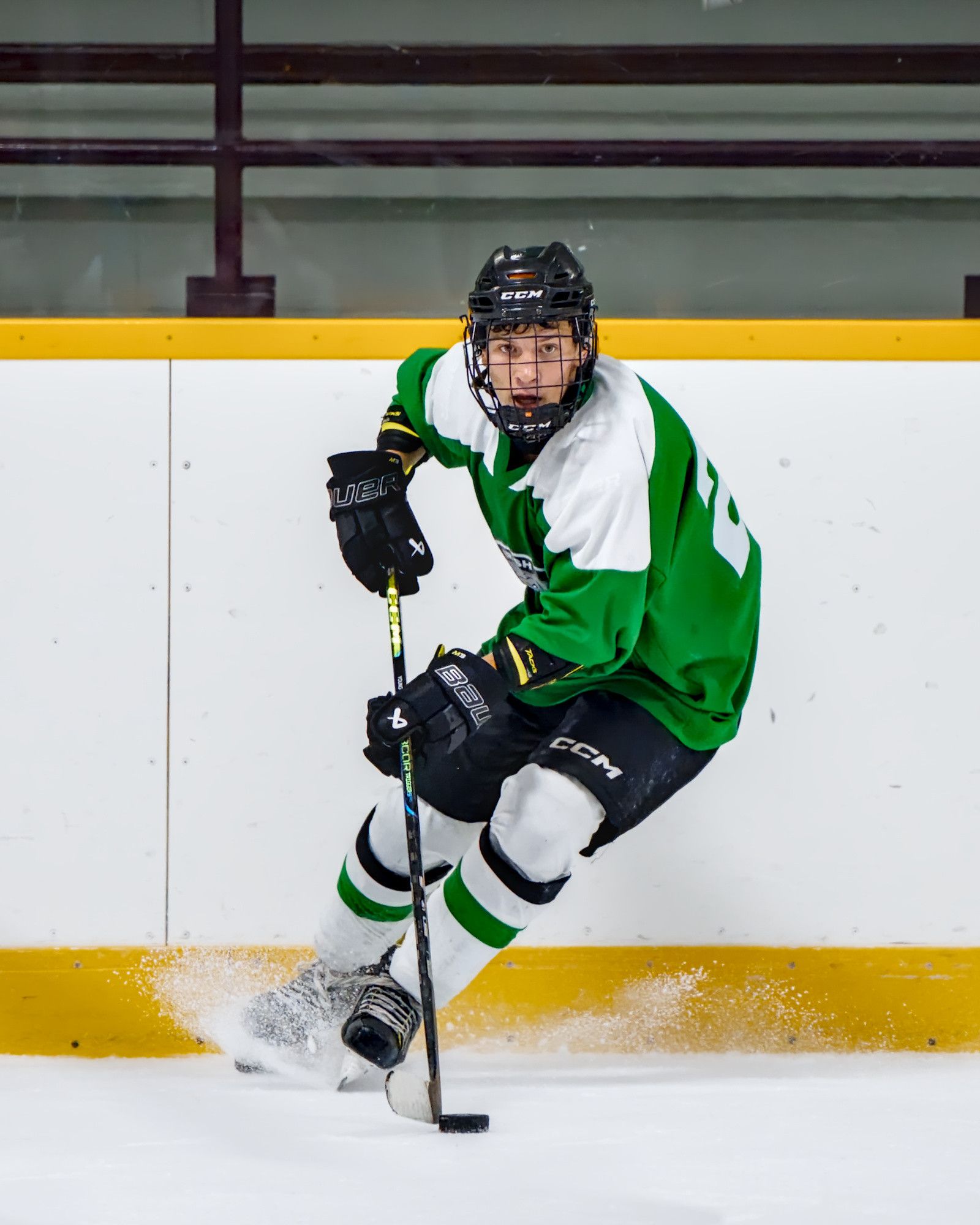 A skater cuts back hard in front of the boards, throwing a spray of ice off his blades.