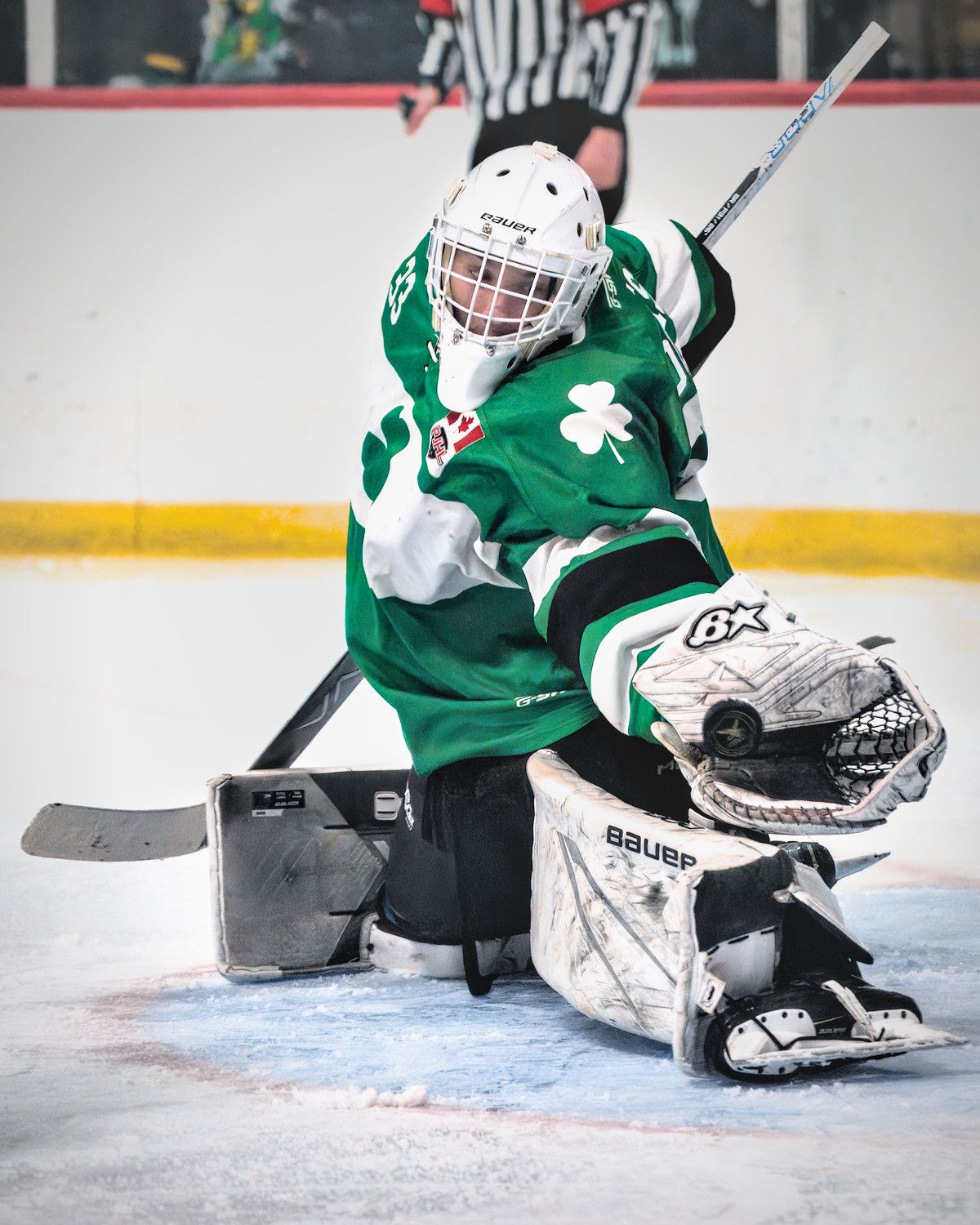 A goaltender in a green shamrock jersey turns into the shot and reaches out to his side with the catching glove.