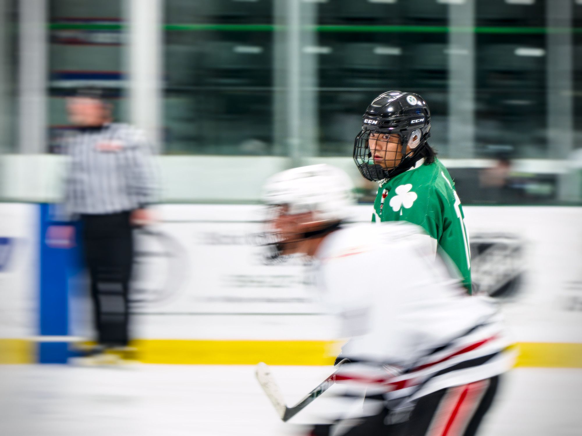 A panned frame streaks the boards and a passing opponent into motion blur while the skater in green stays sharp.