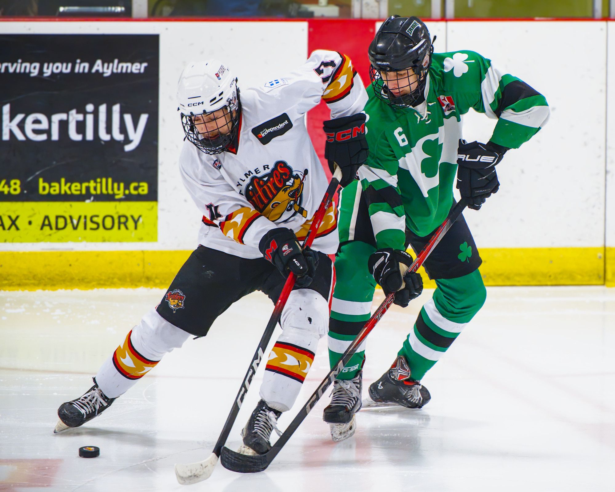 Two players cross sticks low over a loose puck, shoulder to shoulder in front of the boards.