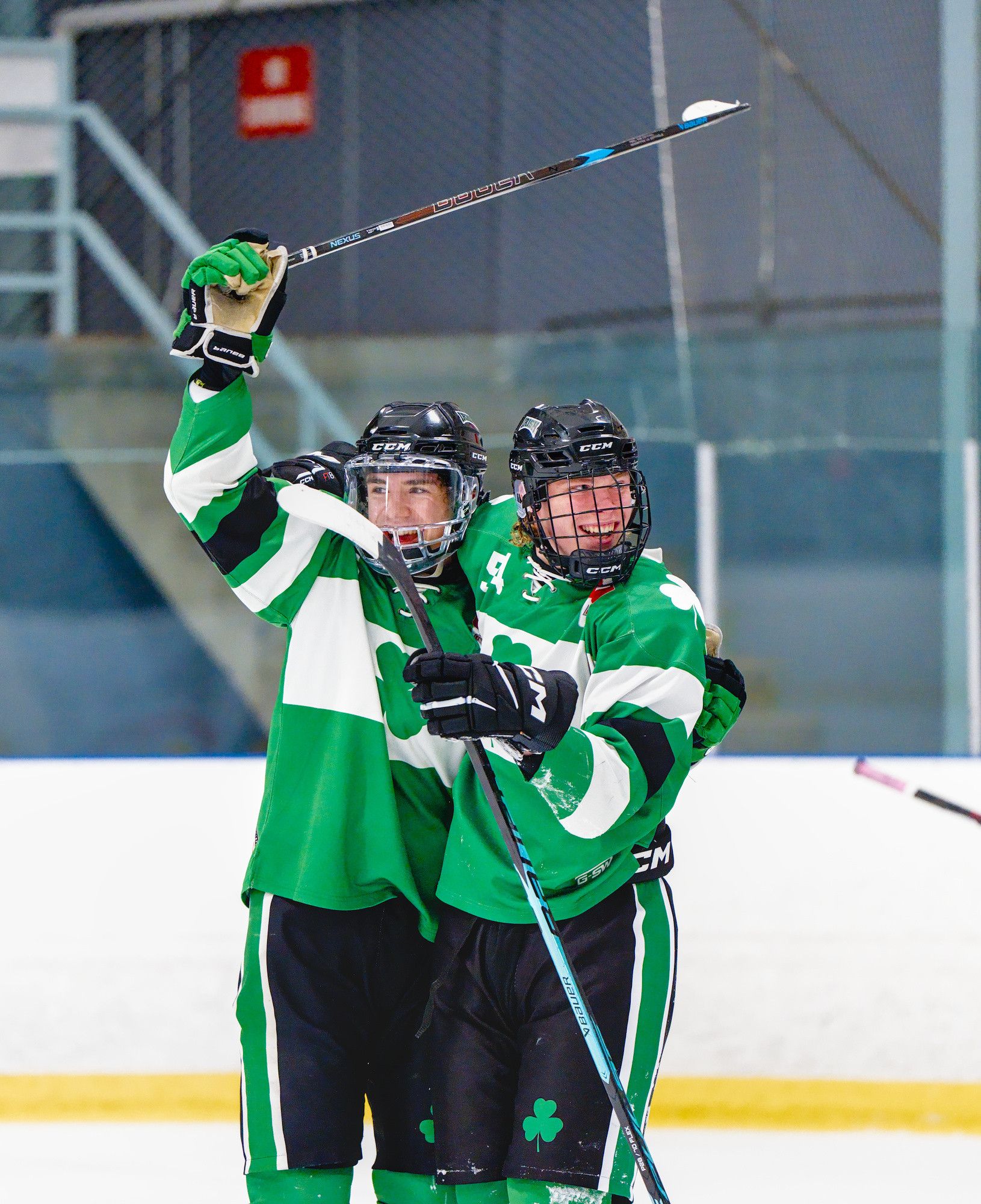 Two teammates in green jerseys pull each other into a hug after a goal, one stick raised over their heads.